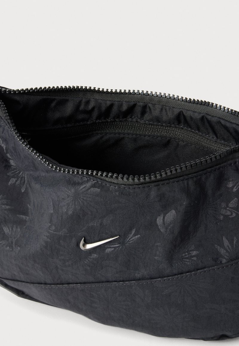 Schwarzes Stoffetui mit dezenter Blumenmusterung, silbernem Nike-Logo und teilweise geöffnetem Reißverschluss, der ein Innenfach mit einer weiteren Reißverschlusstasche zeigt.