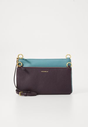 Két színű bőr keresztpántos táska türkiz és sötétlila színben, arany gyűrűkkel, cipzáras záródással és állítható pánttal, arany betűzéssel márkázva.