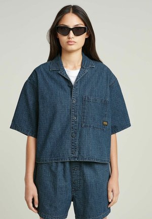Chemise en denim bleu foncé à manches courtes avec un bouton sur le devant, une poche poitrine et une coupe décontractée, associée à un short assorti.