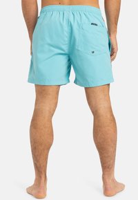 Shorts de bain bleu clair avec une taille élastique. Comprend une poche arrière avec un bouton et des coutures plates pour une finition lisse.