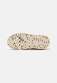 Suela de zapato de goma beige con superficie texturizada, estrías circulares y horizontales, agujeros de ventilación y una impresión de logo cerca del talón.