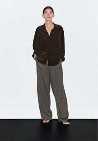 Mørkebrune satin skjorte med knapper foran og løstsiddende grå linnedbukser. Skjorten har en afslappet pasform, og bukserne er vidde med en struktureret overflade.
