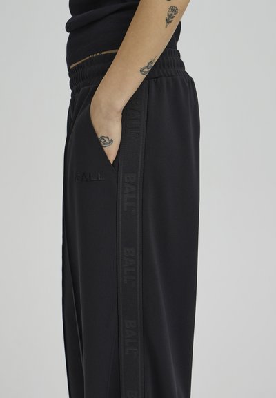 Pantalones deportivos negros con cinturilla elástica, bolsillo lateral y la marca tonal "BALL" en la costura exterior. Tela suave con textura lisa.