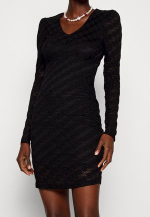 Robe courte noire en dentelle à manches longues avec épaules bouffantes portée par un mannequin, associée à un collier de perles blanches et rouges.
