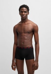 Black boxer briefs with a red "HUGO" logo on the waistband, featuring a fitted design and smooth fabric, worn by a male model.