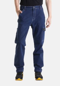 Pantalon cargo en denim bleu avec deux poches latérales et une poche à patch sur la jambe droite, avec des coutures contrastées et une coupe décontractée.