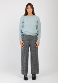 Maglione azzurro chiaro e luccicante con colletto rotondo abbinato a pantaloni a gamba larga grigi a quadri e stivaletti neri alla caviglia.