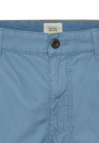 Lichtblauwe shorts van zachte stof, met een knoopsluiting, riemlussen en contrasterende oranje stiksels op de tailleband.
