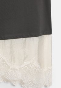 Dunkelgrauer Stoff, der über cremefarbenem, zerknittertem Stoff liegt, mit einem filigranen Spitzenbesatz am unteren Rand.