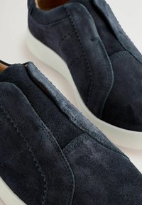 Zapatos de ante azul marino tipo slip-on con costuras texturizadas y acentos laterales elásticos, que cuentan con una suela de goma blanca para contraste y durabilidad.