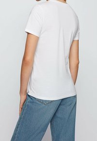 Camiseta blanca de manga corta con escote redondo, hecha de suave material de algodón, ajustada en los hombros y ligeramente suelta en el dobladillo.