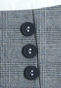 Tissu à carreaux gris et marine avec trois boutons noirs, présentant un tissage texturé et des lignes verticales et horizontales contrastées.