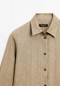 Beżowa lniana koszula z kołnierzykiem, z czarnymi guzikami i metką z napisem "Massimo Dutti" przy dekolcie. Prosty i elegancki design.