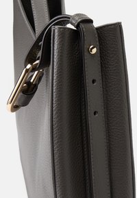 Sac à main en cuir texturé gris avec un clip en métal doré, une bandoulière plate, et des coutures visibles le long des bords.