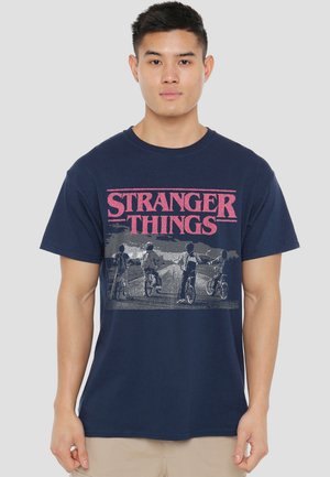 Navy blue cotton t-shirt featuring a graphic print of four figures on bicycles with the text "STRANGER THINGS" in bold pink lettering.