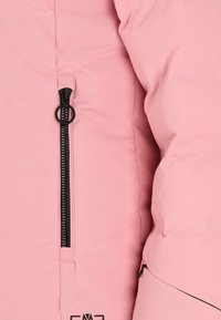 Ljusrosa puffjacka med en synlig svart dragkedjeficka och slät textur; har en rundad söm och logotyp vid fållen.
