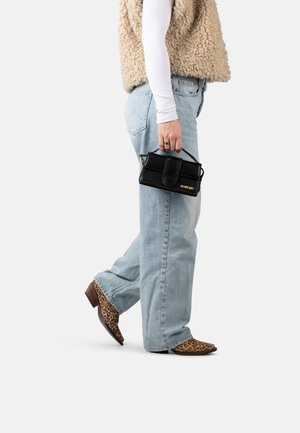 Piccola borsa a tracolla in pelle nera con manico superiore, design rettangolare, dettaglio del logo dorato e chiusura con zip, abbinata a jeans azzurri e stivali con stampa leopardata.