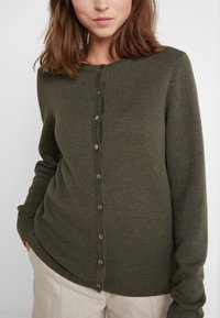 Cardigan vert olive en tricot doux, avec un devant à boutons, des poignets côtelés et une texture lisse.
