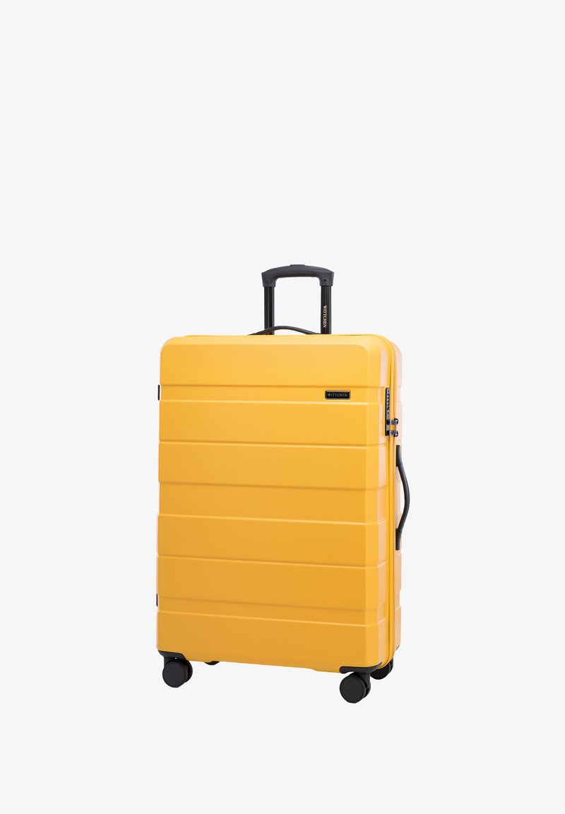 Žlutý tvrdý kufr s vertikálními drážkami, černou teleskopickou rukojetí, boční rukojetí a čtyřmi hladkými koly pro snadnou manipulaci.
