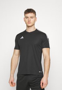 Zwart sportshirt met korte mouwen, een V-hals ontwerp en witte strepen langs de schouders, gemaakt van lichtgewicht stof.