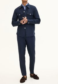 Navy blue two-piece outfit featuring a button-up jacket with chest pockets and matching trousers, made from textured fabric.