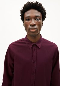 Camicia button-up di un elegante bordeaux scuro con colletto a punta, caratterizzata da una sottile trama e un logo ricamato sul lato sinistro del petto.