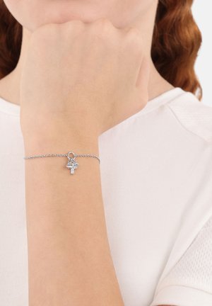 Bracciale in argento con un piccolo ciondolo a forma di fiore e croce. Il bracciale presenta uno stile delicato e minimalista.