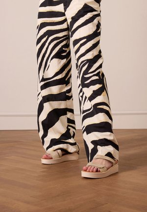 Wide-leg pants in a bold black and white zebra print, paired with beige platform sandals featuring textured straps.