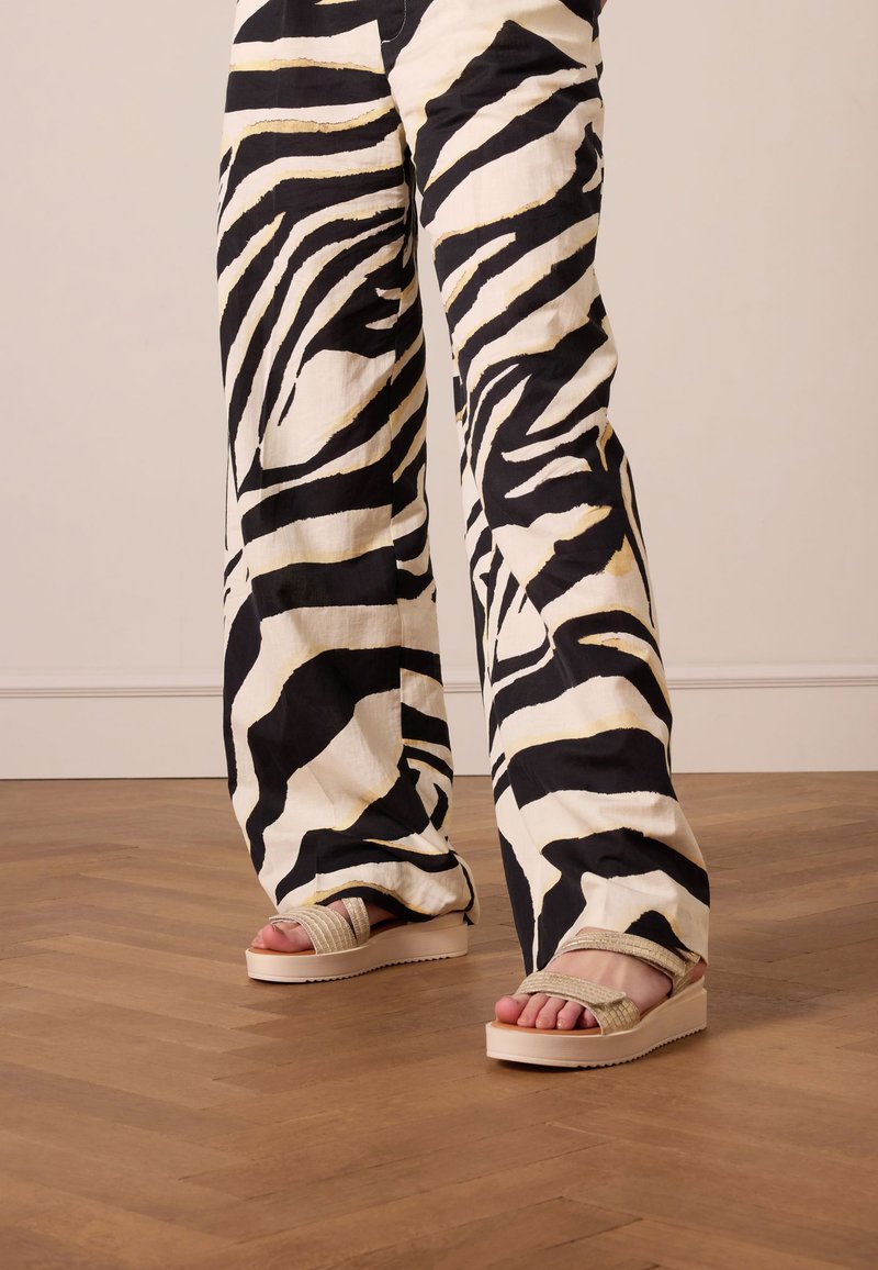 Wide-leg pants in a bold black and white zebra print, paired with beige platform sandals featuring textured straps.