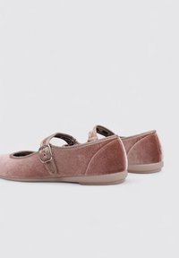 Bailarinas de terciopelo rosa suave con una correa al tobillo y detalle de hebilla, punta redondeada y una suela de goma beige flexible.