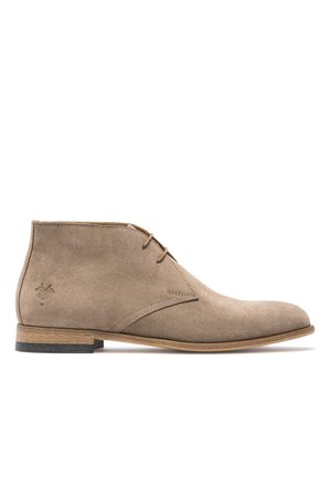 Bottine en suède beige avec un bout rond, deux œillets et une semelle en bois brun. Comprend un design en couture et un logo en relief sur le côté.