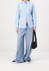 Ljusblå randig skjorta med knappar i bomull, i kombination med stora ljusa jeans i denim. Svart axelväska och svartvita sneakers.