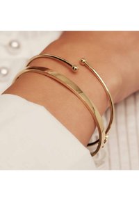 Goudkleurige metalen armbanden om een pols, waaronder een platte band, een gladde ronde vorm en een open ontwerp met een kleine balaccent.