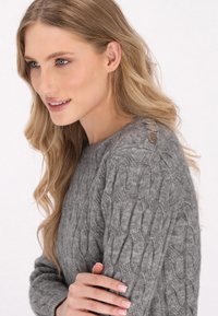 Grauer gestrickter Pullover mit einem Kabelmuster, Rundhalsausschnitt und dekorativen Knöpfen auf der Schulter. Weicher Stoff, lange Ärmel.