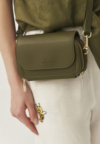 Olivengrøn læder crossbody taske med struktureret overflade, guldhardware, lynlåslomme og klaplukning. Bemærkelsesværdig accent: bi-patch på tøjet.