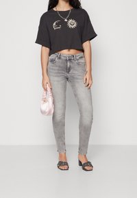 Camiseta negra corta con gráfico de luna y sol, jeans ajustados grises, sandalias negras deslizables y bolso de satén rosa. Collar de cadena de plata simple.