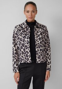 Veste courte à imprimé léopard en beige et noir, avec un col et une fermeture à boutons, portée sur un top noir à côtes.