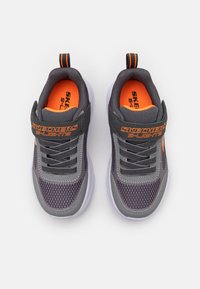 Zapatillas deportivas grises con parte superior de malla, acentos naranjas y correa negra. Suela de color claro. Textura con patrón en los laterales para mayor transpirabilidad.