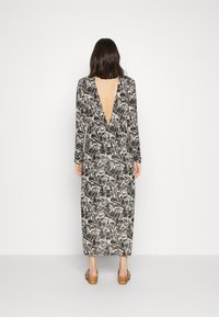 Vestido longo preto e branco com padrão, com decote em V profundo nas costas, mangas longas e silhueta ajustada. Feito de um tecido texturizado.