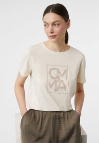 Cream-colored t-shirt with a round neckline and short sleeves, featuring a graphic design in dotted metallic accents.