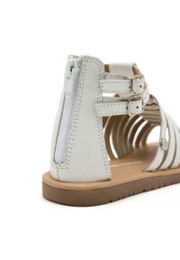 Sandalo bianco in pelle con design aperto, chiusura con zip sul retro, due cinturini regolabili con fibbie e suola in gomma marrone.