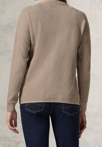 Beige texturerad tröja med långa ärmar, ribbat avslut och rund halsringning, kombinerad med mörkblå jeans i klassisk stil.