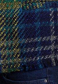 Pull en tricot avec motif à carreaux multicolores dans des tons bleus, verts et gris. Tissu texturé avec ourlet côtelé et bords frangés.