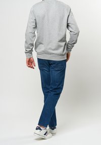 Gray sweatshirt with long sleeves and ribbed waistband, paired with blue jeans and white sneakers featuring navy and red accents.