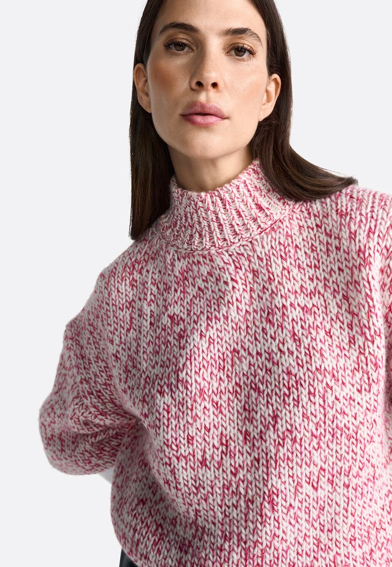 Strickpullover in Pink und Weiß mit hohem, geripptem Kragen. Chunky-Textur und lässige Passform. Verfügt über ein dezentes Muster im gesamten Design.
