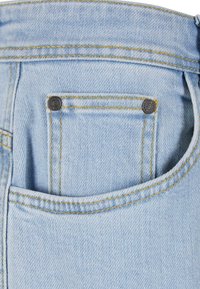 Lys blå denim jeans med en synlig baklomme og kontrastfarget gul søm. Har en liten dekorativ svart knapp.