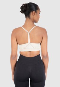 Beige urheiluliivi, jossa on urheilutoppi ja kapea olkaime, sekä teksturoitu vyötärönauha. Yhdistetty korkeavyötäröisiin mustiin legginsseihin.