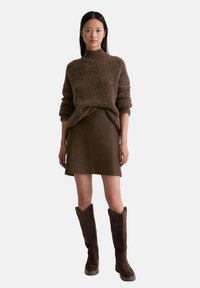 Brązowy sweter z teksturowanej dzianiny o wysokim kołnierzu, w zestawieniu z dopasowaną brązową spódnicą i brązowymi zamszowymi botkami do kolan.