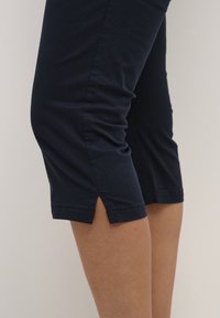 Námořnické modré capri kalhoty vyrobené z měkké bavlněné směsi, s přiléhavým střihem, bočními rozparky na lemu a viditelnými švy.