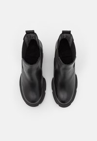 Pár černých kožených kotníkových bot na slip-on s kulatými špičkami a poutky na vytahování, zobrazených shora na bílém pozadí.